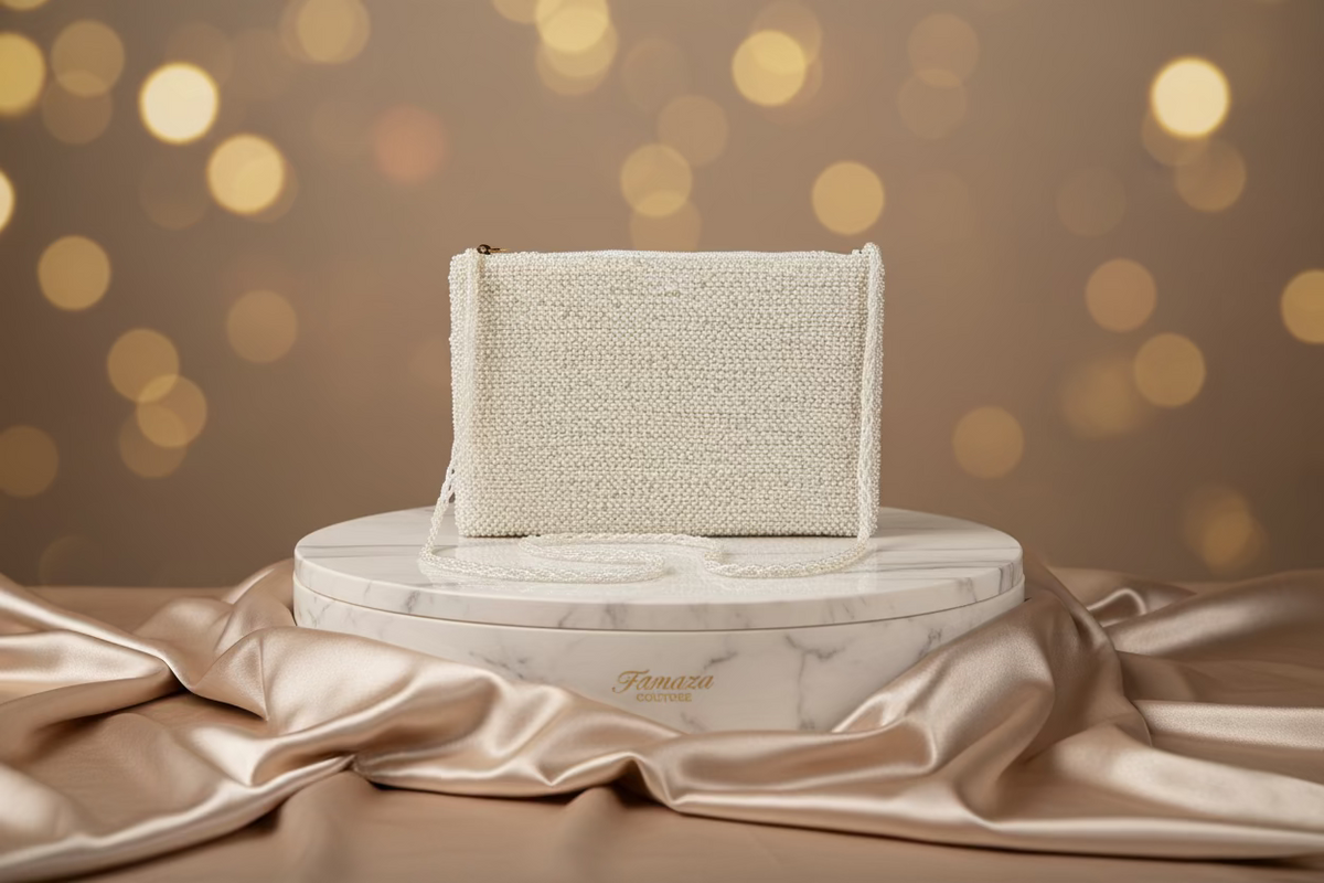 A white clutch bag with glass bead embroidery, featuring a chain strap and a zipper closure.