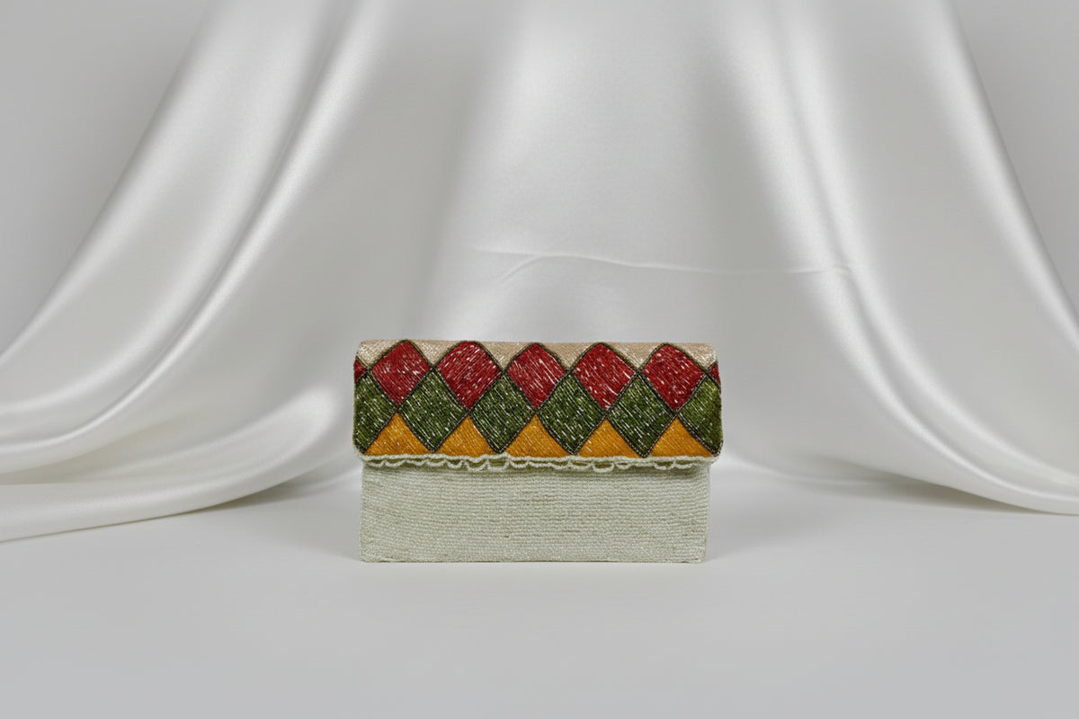 A white clutch bag with multi-coloured nano glass beads patterns, hand embroidered, displayed outdoors.