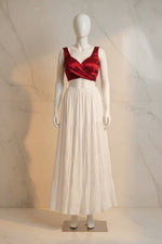 A white tiered skirt with embroidered details and a lace hem, hanging on a hanger against a dark mesh screen and a light wall.