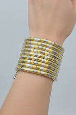 A wide cuff bracelet made of alternating yellow and silver-toned rectangular links, worn on a person's wrist against a black background.