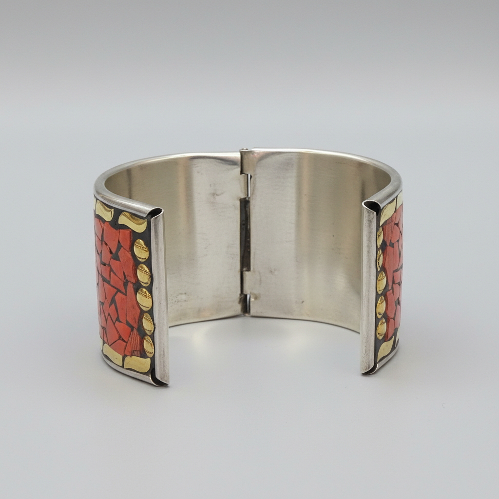 A wide silver cuff bracelet with red and gold mosaic inlay panels on the outer sides, photographed on a light gray studio background.