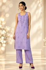 A woman modeling a lavender purple embroidered kurta and matching wide-leg trousers against a white patterned backdrop.