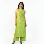 A woman modelling a lime green sleeveless kurta with matching green pants, standing against a white patterned backdrop.