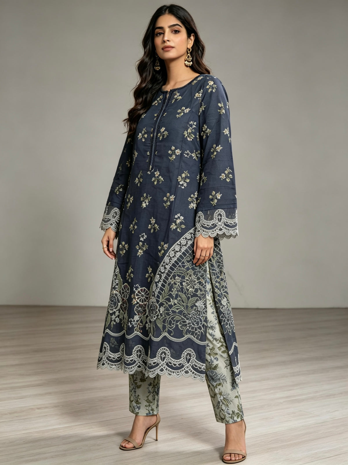 A woman modelling a navy blue three-piece kurta set with beige floral prints and lace trim, paired with matching pants and beige high-heeled sandals, set against a neutral studio background.