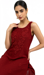 A woman modelling a sleeveless deep red embroidered kurta with floral embroidery on the bodice, set against a plain white background.