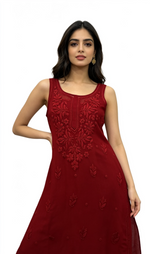 A woman modelling a sleeveless red anarkali dress with intricate floral embroidery on the bodice and scattered embroidery on the skirt, set against a plain white background.