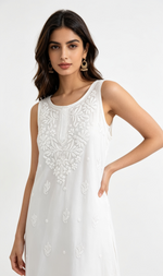 A woman modelling a sleeveless white dress with intricate floral embroidery on the bodice and scattered embroidered motifs down the skirt, set against a plain white studio background.