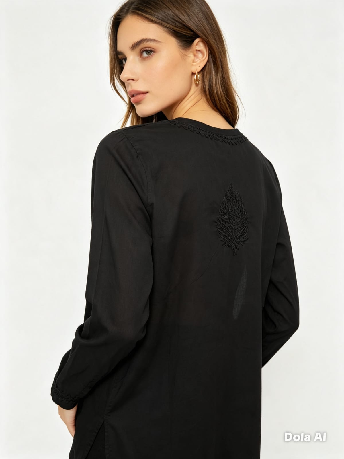 A woman shown from the back wearing a black long-sleeve tunic top with a subtle tonal embroidered motif on the upper back, photographed against a clean white studio background.