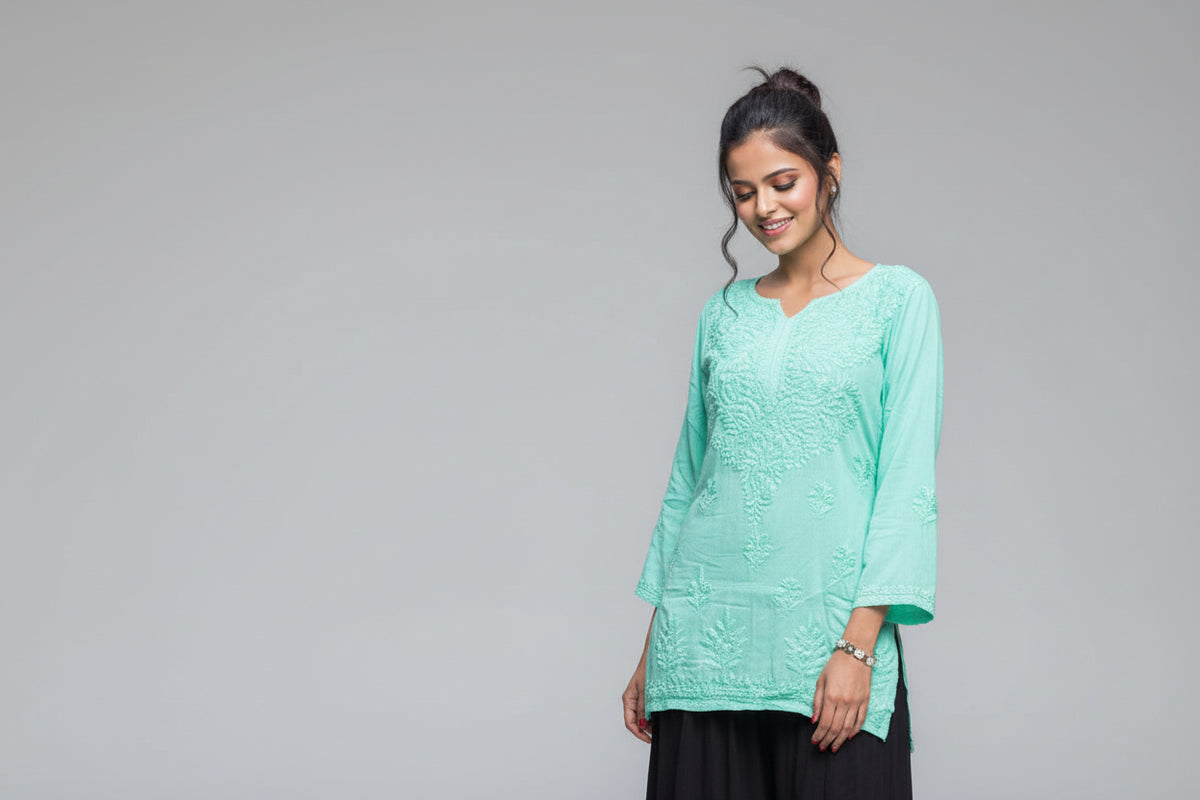 A woman standing in a garden wearing a traditional turquoise chikankari short kurti with black gharara with flared hand embroidery