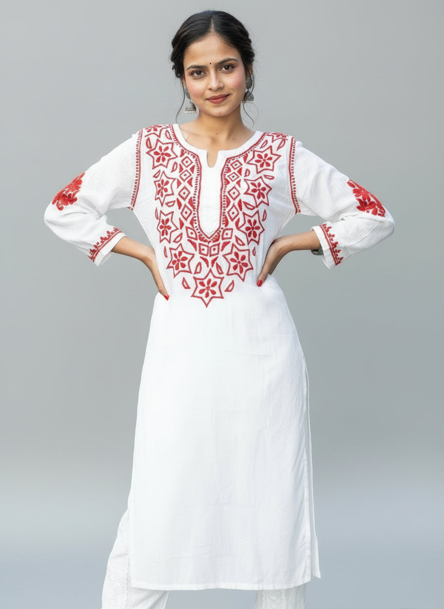 A woman standing in a garden wearing a white and red embroidered kurti with long sleeves.