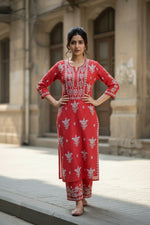 A woman standing on a sidewalk withwearing a red colour traditional Lucknowi chikankari kurti with floral patterns and palazzo pants, holding a bag.