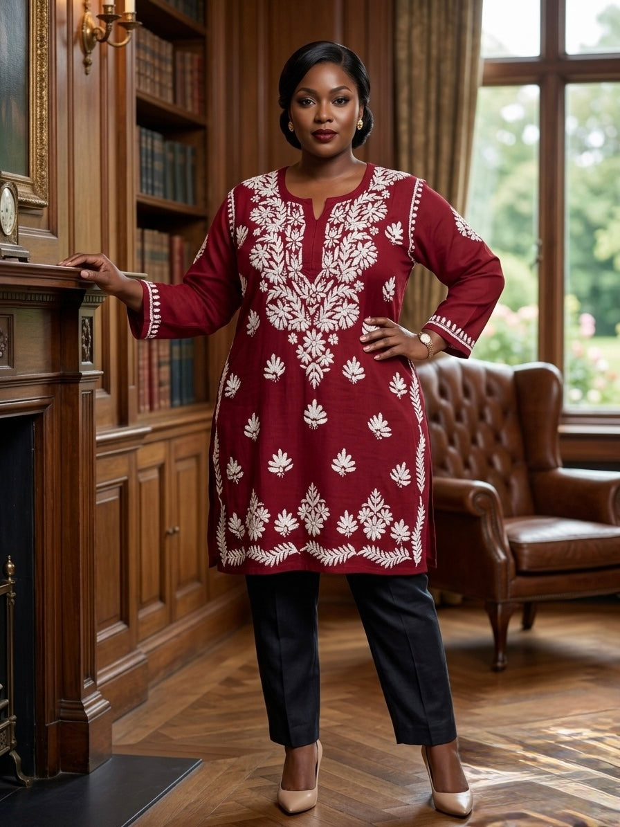 A woman stands in a warm, wood-panelled room wearing a maroon long kurta with white floral embroidery, paired with black trousers and beige heels.