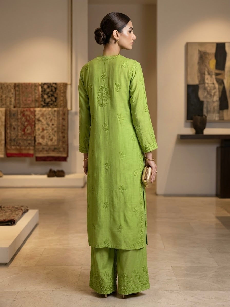 A woman stands with her back to the camera wearing a bright lime green embroidered kurta and matching wide-leg trousers in a modern, well-lit gallery space.