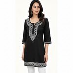 A woman modeling a black three-quarter sleeve kurta with white geometric embroidery around the neckline, sleeve cuffs, and hem, paired with white pants against a plain white background.