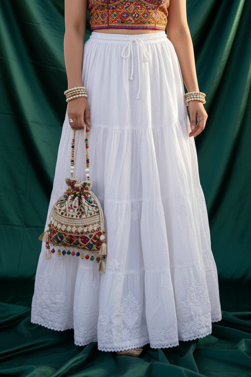 A woman wearing a long white tiered maxi skirt white rayon skirt with white Ghasspati hand embroidery on the bottom two layers and the hem is adorned with white crochet lace.