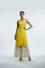 A yellow sleeveless dress displayed on a white mannequin inside a store. The dress has a textured bodice and a layered, ruffled skirt in a light cream or off-white colour.