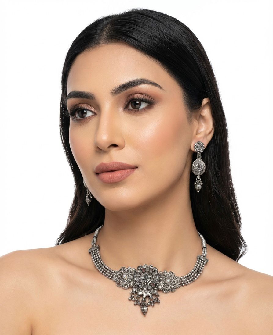 A young woman wearing a detailed oxidised silver choker necklace with a central floral medallion and matching tiered drop earrings.
