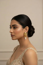 A young woman wearing vintage-inspired brass jhumka drop earrings, featuring a central pink cabochon stone surrounded by delicate white pearl accents and antique brass detailing.