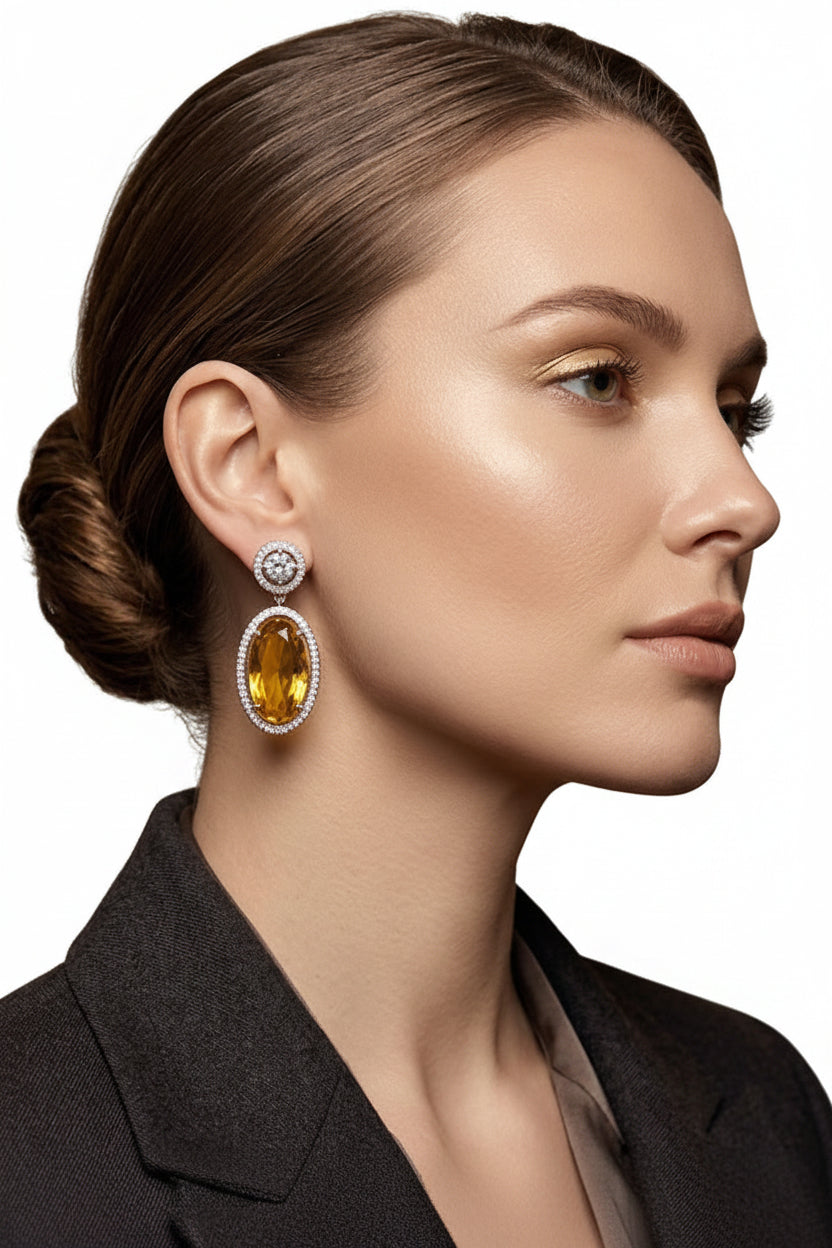 Luxurious oval yellow citrine drop earrings set in sterling silver with pave diamond halo accents, hanging against a soft, unfocused opera house-inspired gold velvet background.