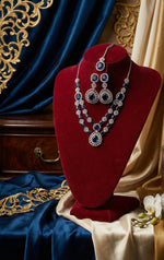 American Diamond necklace , earrings and maag tikka displayed on a red velvet stand with ornate background.