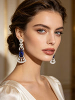 A pair of silver-toned Art Deco style drop earrings with marquise-cut deep blue gemstones and pavé-set clear accent stones, displayed on a black card against a dark background.