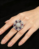 Silver-tone floral halo ring with oval purple stones, round AD center, and marquise accents — shown on hand against black velvet.