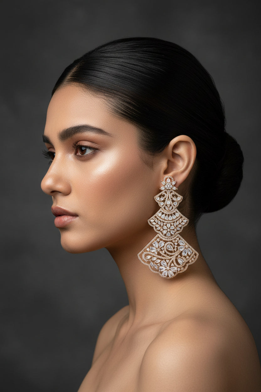 An ornate gold-toned brooch featuring intricate filigree cutouts and clear teardrop and round stones, displayed on a textured black background.