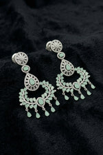 A pair of luxurious chandelier-style dangle earrings in a serene Aqua Mist hue, elegantly displayed on a textured black velvet surface, featuring intricate rhodium-plated brass and brilliant-cut stones.