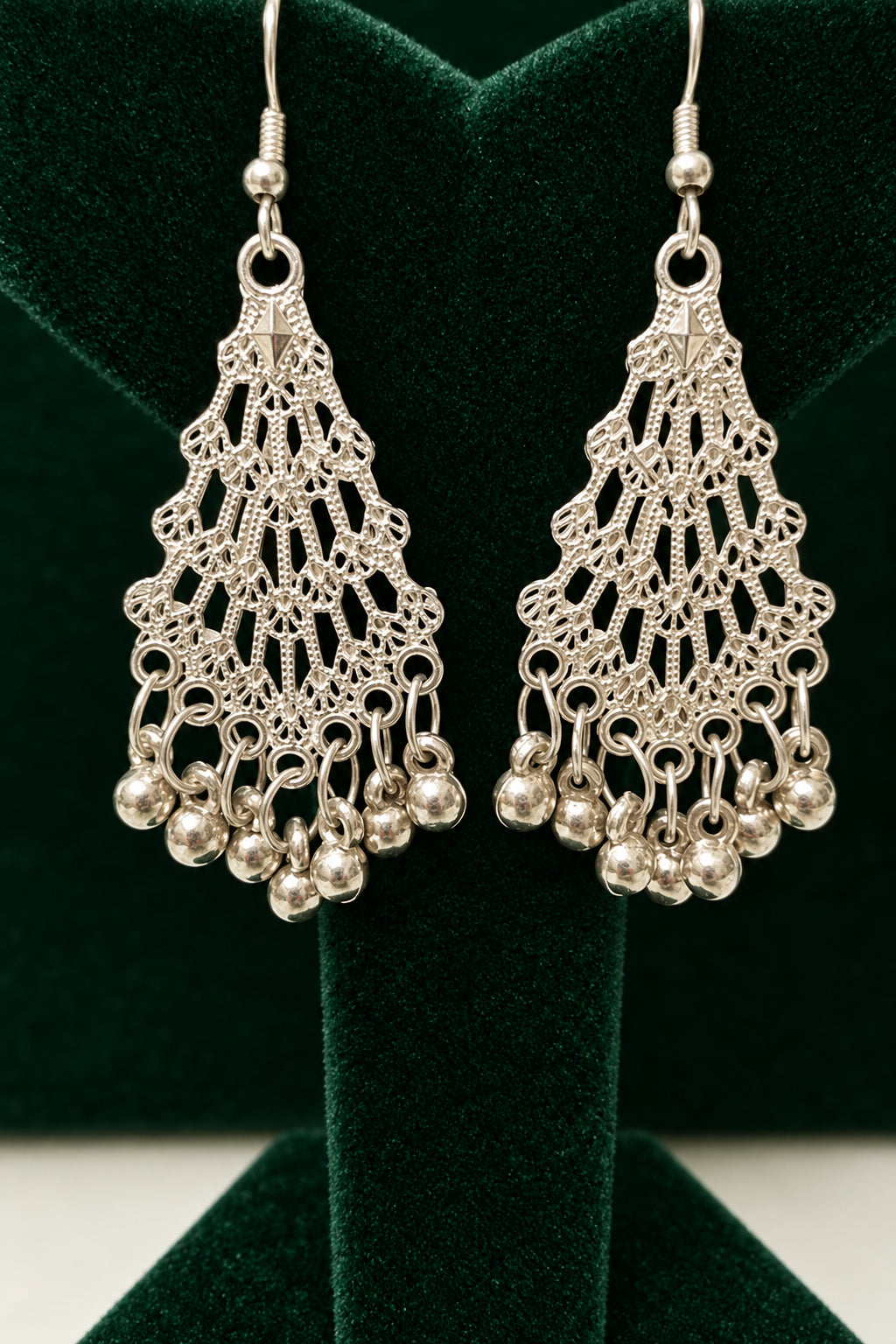 A pair of silver-toned filigree dangle earrings with small hanging beads, displayed on a black jewelry stand against a black background.