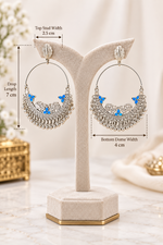 Oxidized silver-plated hoop earring featuring intricate peacock motifs with vibrant blue enamel accents and dangling ghungroo bells, displayed on a black stand