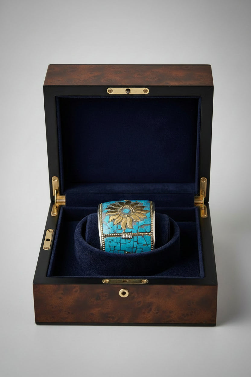 A stunning wide cuff bracelet featuring a detailed gold-tone sunburst design set against a mosaic of vibrant turquoise stone fragments, presented inside a luxurious dark blue velvet-lined wooden jewelry box.