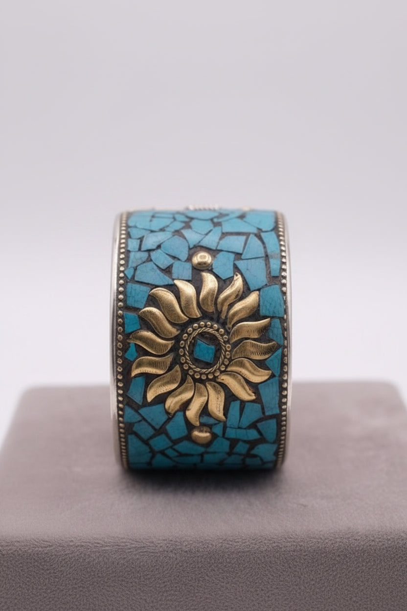 A vertical close-up shot of an artisanal, wide cuff bracelet featuring a detailed golden sunburst center surrounded by vibrant turquoise mosaic fragments, resting on a gray display block with a semi-transparent scale graphic indicating a width of 4.5 cm.