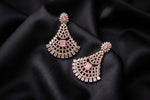A pair of ornate gold-toned chandelier earrings with pink stone accents, displayed on a draped black satin fabric background.