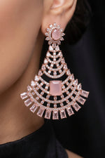 A close-up of a model wearing a large, ornate rose gold dangle earring adorned with clear crystals and a central pink stone.