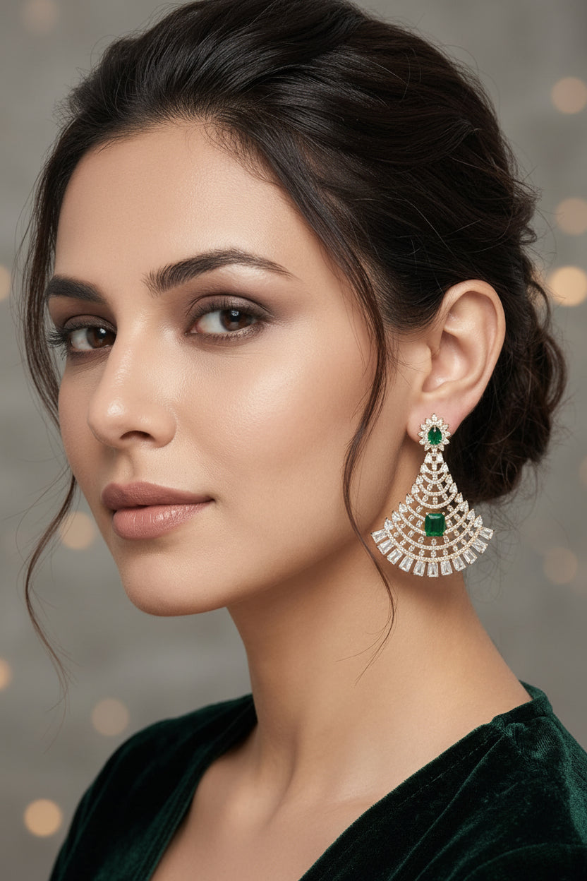 A woman wearing a large, ornate silver-toned chandelier earring with green stone accents, shown in a close-up portrait against a light gray background.
