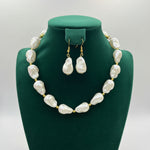 A jewelry set featuring a statement necklace of large, irregular white baroque pearls with gold-tone spacer beads and matching drop earrings, displayed on a black mannequin bust.