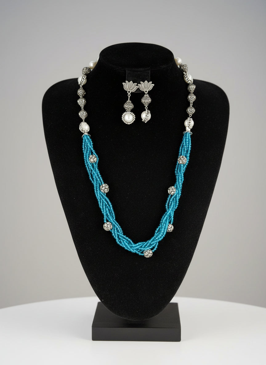 Beaded mala with silver and pearl beads in on both sides start and drop is designed with sky blue colour glass nano bead and silver ball beads, along withLotus design earrings with silver and pearl beads in drop. Oxidised party wear jewellery set.