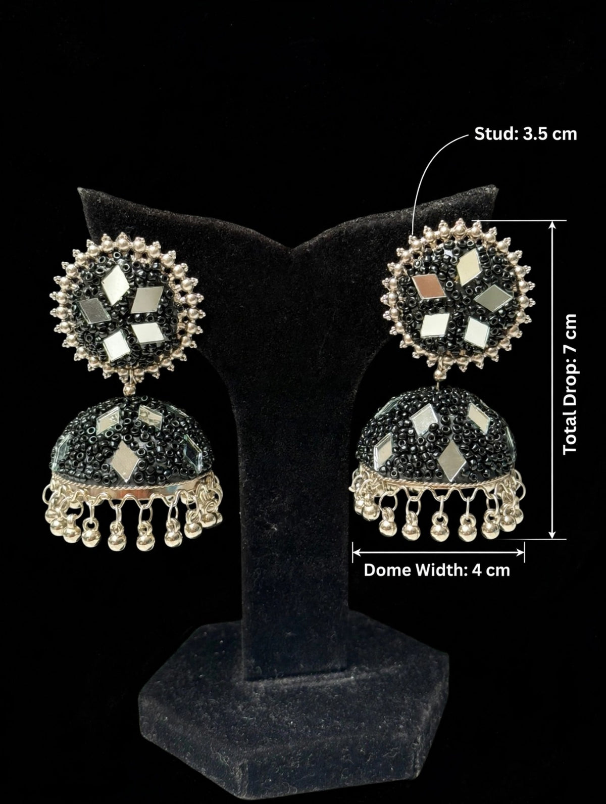 Black mirror bead jhumka — 7cm total drop, 3.5cm stud, 4cm dome — silver-tone ghungroo trim, multi-shape mirror inlays, displayed on black velvet stand — Famaza Couture.