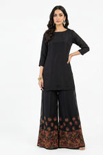 A model wearing black wide-leg palazzo pants featuring vibrant multi-colored floral embroidery at the hem.
