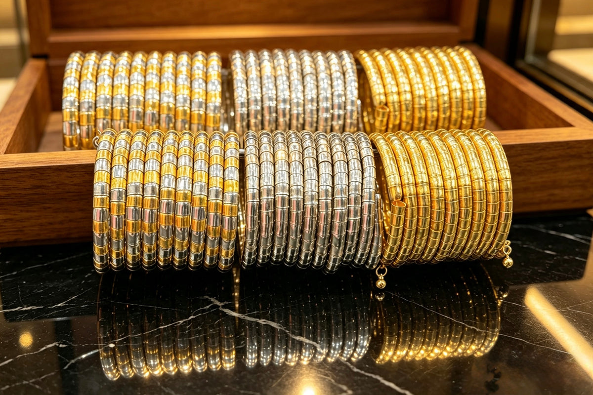 Three stacks of metallic bangles in yellow gold and silver-tone finishes displayed on a wooden stand over a black marble surface, with reflections below.