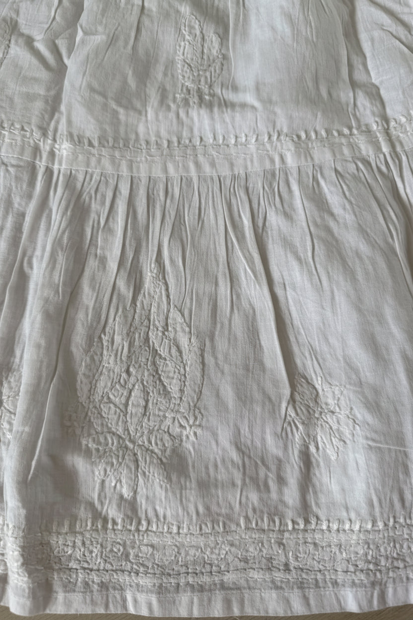 Close-up of a white embroidered fabric garment, showing textured embroidery and gathered seams.