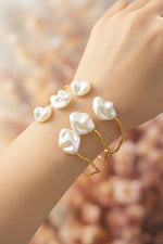 Close-up of a young woman wearing a shimmering 14k gold-plated Mother of Pearl inlay cuff on her wrist, styled with a linen summer dress.