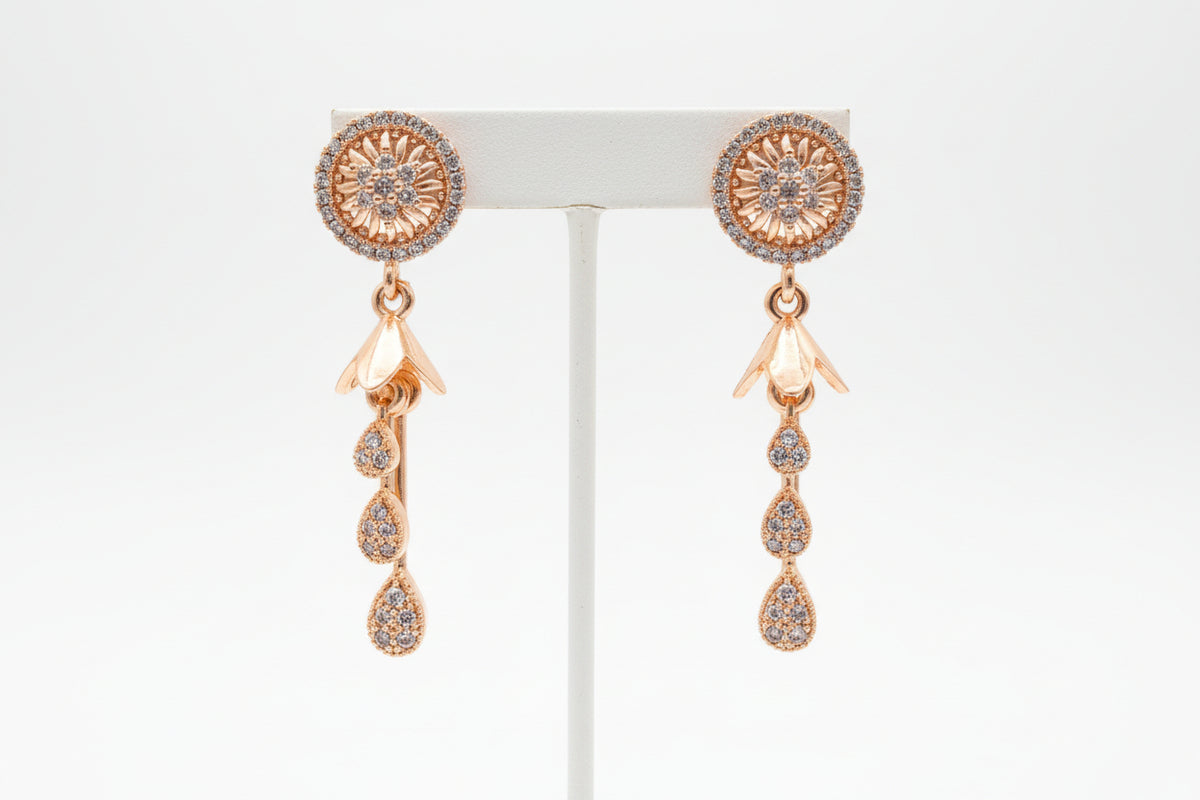 Close-up of golden brass earrings featuring a circular floral stud encrusted with crystals and a three-tier crystal teardrop dangle.