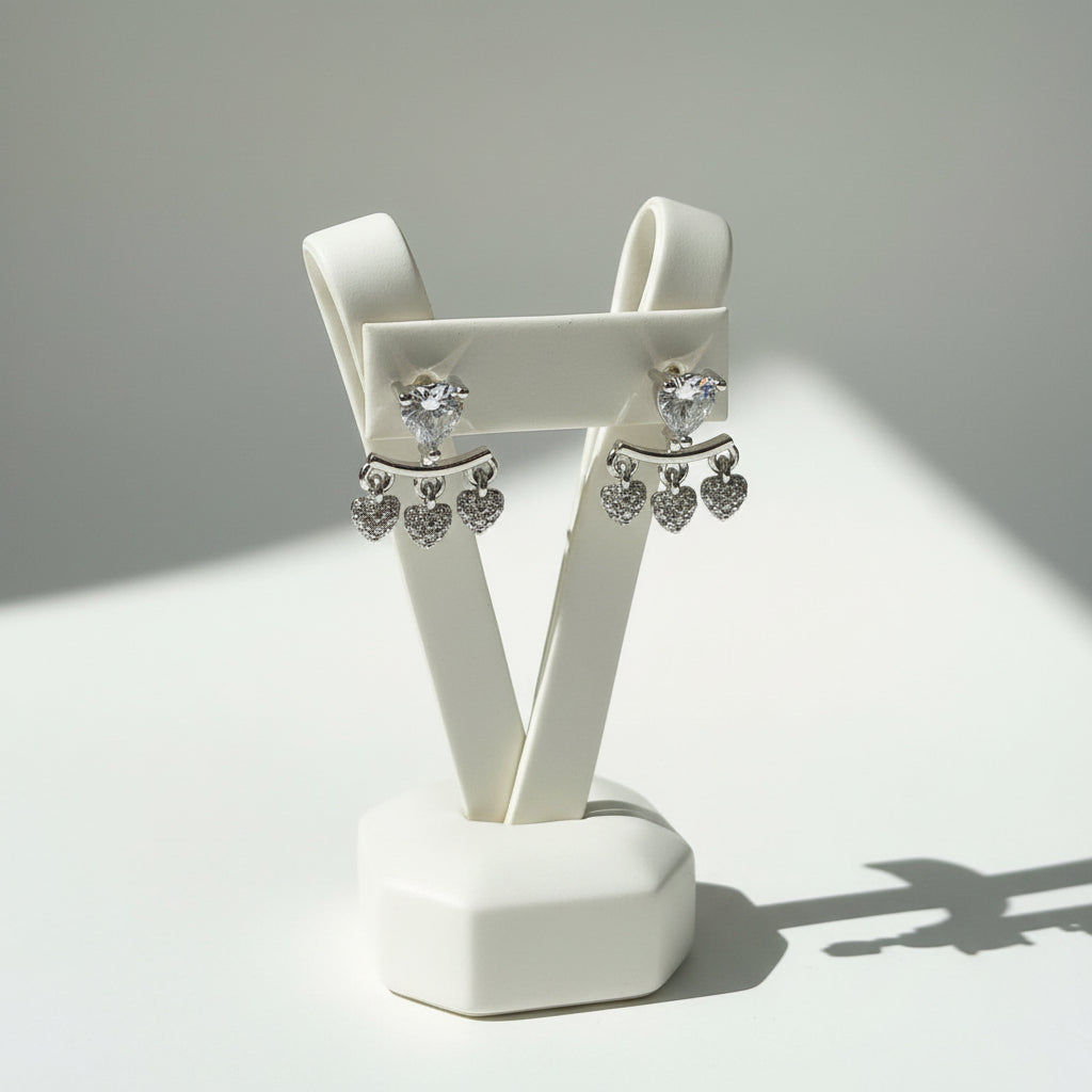 Close-up of the 1cm Amara silver AD earrings featuring a large heart stud and three dangling pavé-set heart charms.