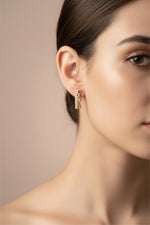 Close-up of the 2cm Aura rose gold AD earrings featuring a vertical stone-set bar and an intertwined infinity wave.