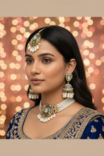 Close-up shot of a woman wearing a handcrafted brass choker set featuring vibrant multi-colored sugar stones and white Kundan embellishments. The necklace is finished with dangling pearl drops, paired with matching statement earrings.