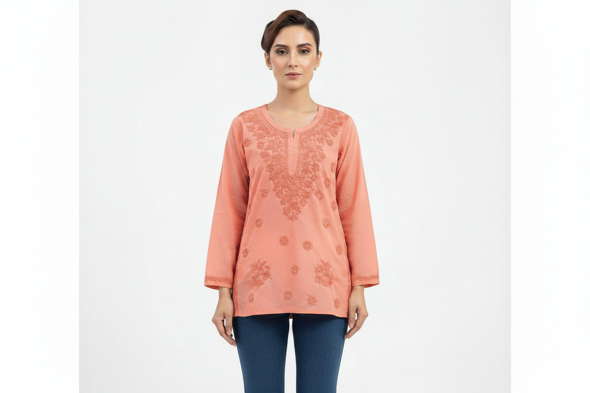 A model wearing a peach-colored short kurti featuring intricate tonal embroidery around the neckline and front, with an inset highlighting the square hemline detail