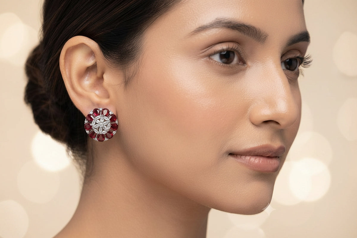 A close-up of a woman wearing a single floral stud earring with red gemstones and a silver-toned center, shown against a soft light gray background.