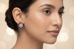 A close-up of a woman wearing a single floral stud earring with red gemstones and a silver-toned center, shown against a soft light gray background.