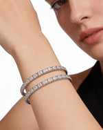A lifestyle close-up of a woman's wrist wearing a pair of sleek, silver-plated American diamond bangles with a single row of shimmering stones in a square-prong setting.